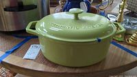 Full view of light green enameled Dutch oven with lid on wooden surface. Shows overall shape and color.