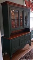 Full front view of the green painted wooden Ethan Allen hutch with glass paneled doors and wooden top surfaces