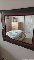 Full face view of the rectangular mirror hung on a wall with a bed and dresser reflected in the glass.