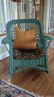 Front view of the green wicker rocking chair with brown pillow and floral seat cushion.