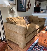 Side view of the brown upholstered sofa showing the rolled arm and removable cushions with pillows and arm protectors.