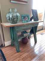Front angle view of distressed green sawhorse table with natural wood top showing details of the weathered paint and wood grain.