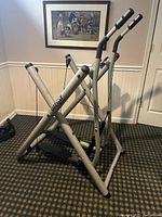 Side angle view of silver Tony Gazelle elliptical showing black handles, foot pedals, and X-frame design.
