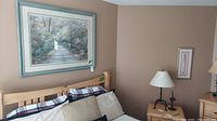 Wide shot showing large framed artwork hanging above a bed, depicting a path through a wooded area with fall colors.