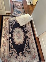 Top view of largest carpet showing floral design with central medallion and border in dark and light colors. Other smaller carpets partially visible.
