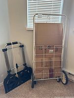 Two hand carts side by side, one white wire-frame with large wheels and one foldable black with telescoping handle.