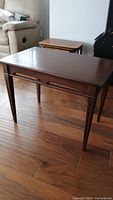 Full view of the solid wood end table showing the top surface and tapered legs with visible scratches.