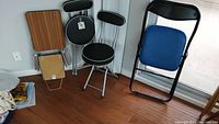 Three folding chairs and two-tiered metal folding table grouped in corner on wooden floor