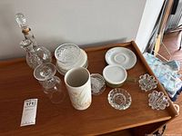 Overview of all items on wooden table showing crystal candle stand, decanter, glass, saucer plates, ceramic cup and ashtrays