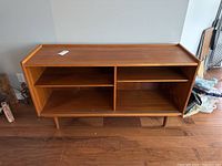 Front view of wooden brown storage cabinet with four open compartments and no doors, standing on four legs.