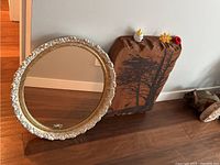 Photo showing round white framed mirror and wooden carving block on floor