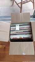 Top-down photo showing a cardboard box filled with multiple vinyl records, some covers visible at the top.