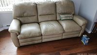 Full view of beige three-seat reclining sofa showing condition and included care kit box on floor.