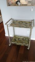 Front angle view showing metal framed tea cart with floral removable trays and wheels.