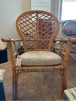 Front view of wicker chair with beige cushion on carpeted floor near window.