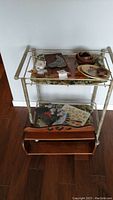 Photo of metal framed wooden hanging shelf with two levels containing wooden bowls, plates, folded textiles and decorative items