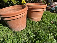 Two terra cotta clay pots positioned upright outside on grass, showing full profile and surface wear.