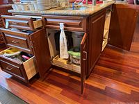 Photo of wooden kitchen island with multiple drawers and cabinets open, showing contents inside.