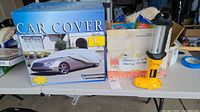 Wide shot of the large car cover box, chamois cloth box, and Dewalt safety light on a table