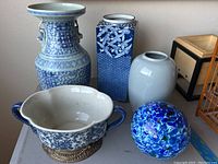 Wide shot showing all five items in the lot together on a surface: three vases, one handled pot, and one glass ball, illustrating overall colors and sizes.
