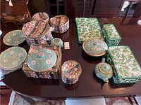 Photo of a wooden table holding a variety of Chinese porcelain items including several lidded serving dishes, round teapot, plates, small containers with intricate floral and geometric pattern designs.