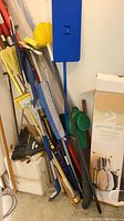 Various cleaning tools leaning against wall with boxed garment rack visible.