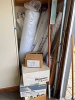 Showing a variety of rolled fabrics leaning against a wall, some wrapped in plastic and paper, boxes stacked at the bottom.