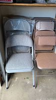 Group shot showing two stacks of folding chairs, one with light grey fabric and one with dusty rose fabric