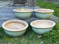 Four green glazed ceramic planter pots arranged on grass in front of wood steps