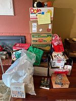 Stacked cardboard boxes primarily labeled as banana boxes, several reusable bags filled with craft supplies, yarn and pattern books visible