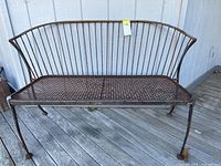 Full front view of the metal garden bench placed on a wooden deck, showing curved backrest and mesh seat surface with rust spots.