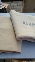 Two cream-colored wool blankets folded, one with partial U.S. NAVY stencil visible