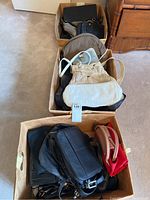 Three boxes filled with assorted handbags and purses seen from above, showing different colors and sizes.