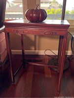 Front view of wooden side table with carved trim and carved pumpkin bowl placed on top.