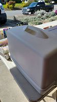 Beige hard plastic carrying case for the sewing machine with handle on top.