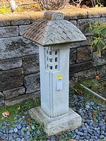 Full view of the stone garden sculpture showing entire lantern shape, tiled roof, and rough stone base.