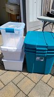 Stack of three large teal 20-gallon storage bins with lids next to a stack of medium white bins and small clear containers.