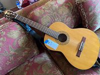 Full front view of classical guitar reclining on couch with strap attached