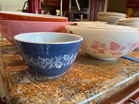 Small blue bowl with white floral design in foreground, larger assorted bowls behind