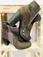 Side view of grey suede ankle boots showing zipper, elastic panel, block heel with metallic accent, and tread on sole.
