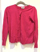 Front view of a bright pink women's cardigan hanging on a hanger against a white background. Long sleeves, knit fabric, button-up style.