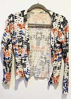 Front view of the cardigan hanging on a hanger showing the full garment with multi-colored geometric and animal print design