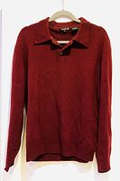Long sleeve wine/garnet cashmere wool sweater hanging on hanger with collar and button placket visible