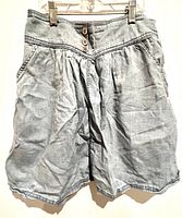 Front view of light blue cotton faux denim skirt with two buttons and pockets, showing gathered pleats and wrinkles.