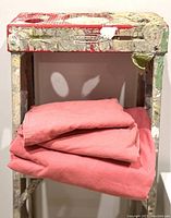 Folded coral duvet cover and pillowcases on a distressed shelf.