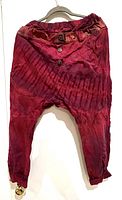 Front view of ruby red tapered harem pants with elastic waistband, button details, and textured tie-dye fabric.
