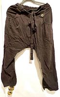Full view of dark brown tapered harem pants hanging on a hanger showing overall shape, waistband, and tapered leg design.
