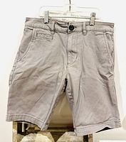 Front view of khaki Bluenotes walking shorts hanging on clear plastic hanger, showing details like button closure, front pockets, and belt loops.