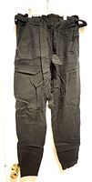 Front view of black linen pants hanging, showing tapered legs, paperbag waist with belt.