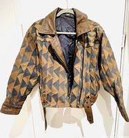 Front view of the jacket showing geometric triangle patchwork in brown and dark grey leather, with zipper and strap belt.